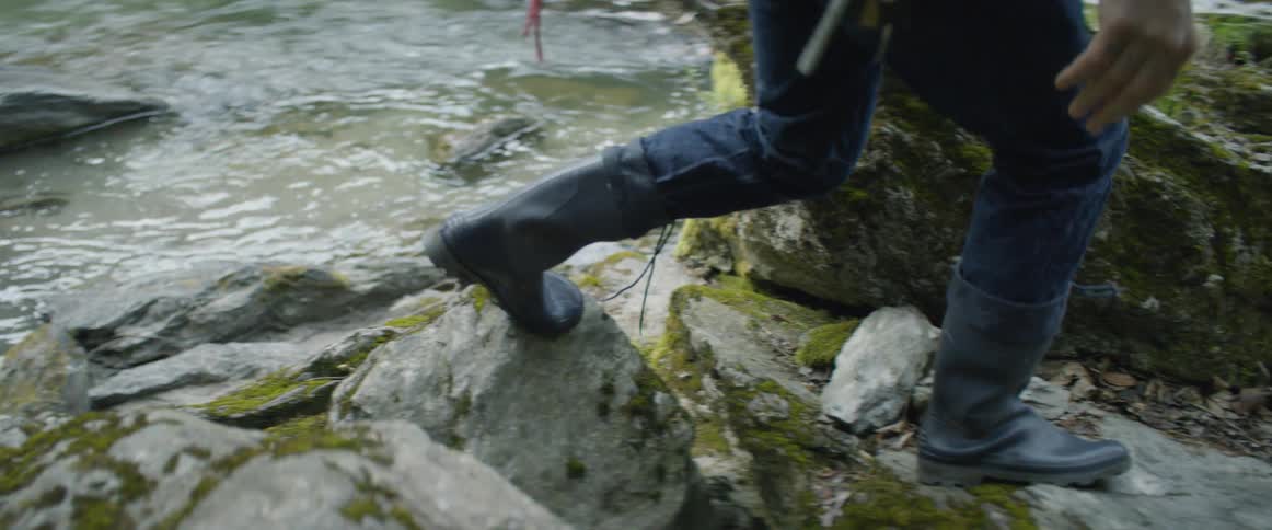 A man climbs up rocks next to a stream