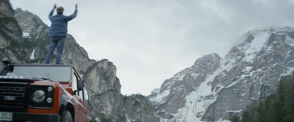 A man stands on a car roof in snowy mountains