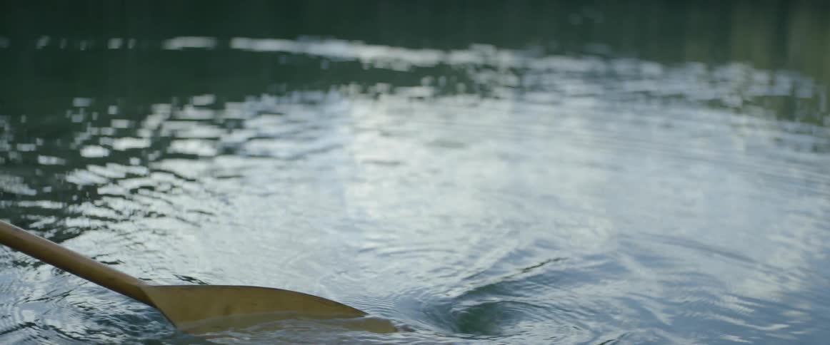 A person paddles in the water with a wooden ore