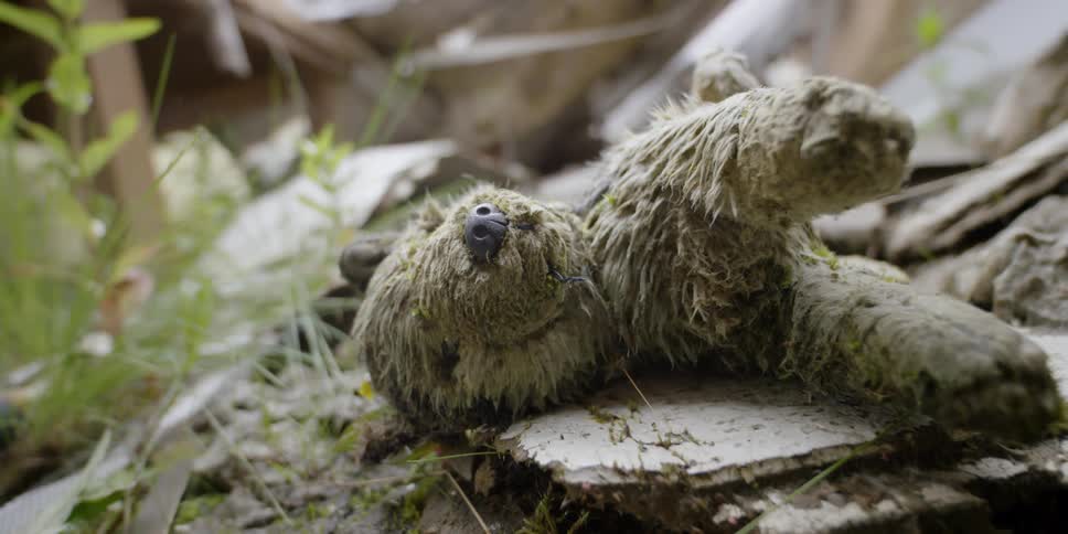 A stuffed toy animal lies discarded on a pile of mud and trash during the day