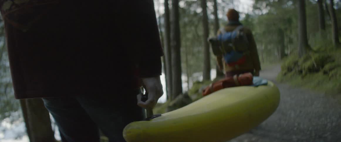Hikers carry a kayak through a forest