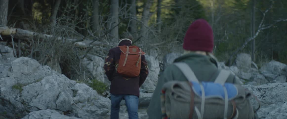 Man and woman wearing backpacks hike through the woods