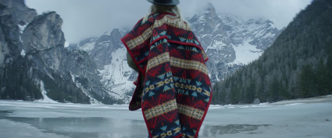 A woman stands next to an icy mountain lake