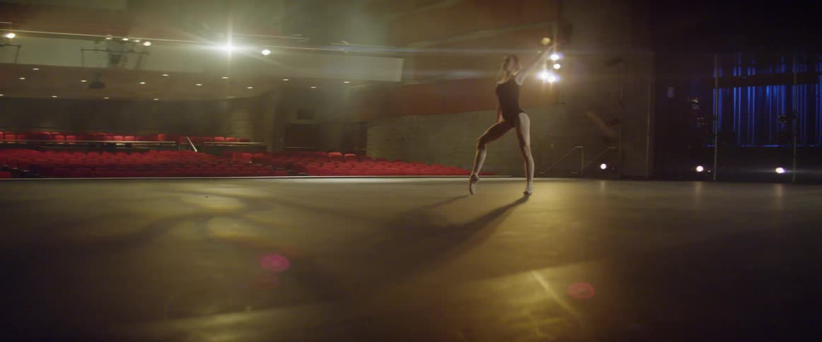 A ballerina is dancing on a stage in an empty auditorium