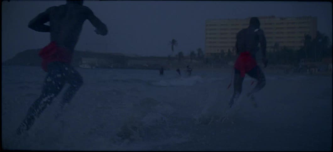 Two men run through choppy waters on the beach