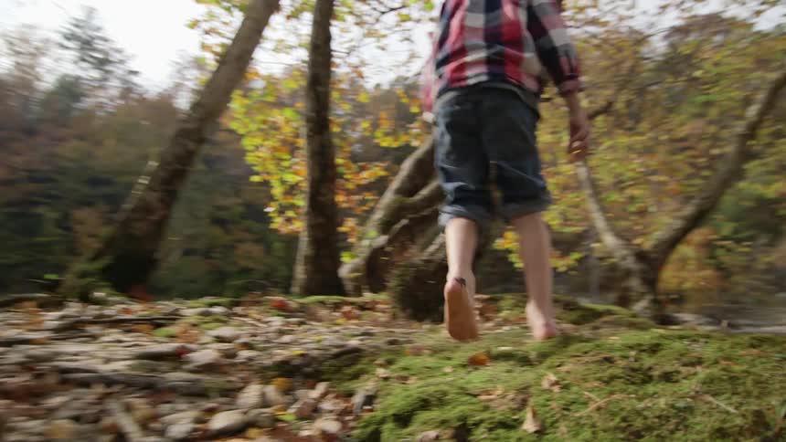 A boy walks barefoot next to a river