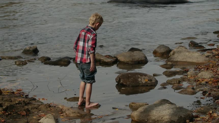 A barefoot boy steps on rocks in the river