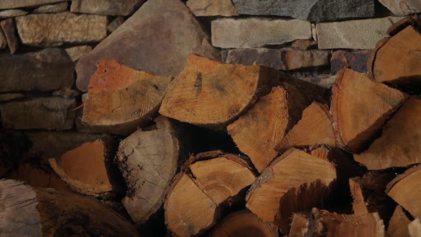 Chopped logs are stacked near a stone wall