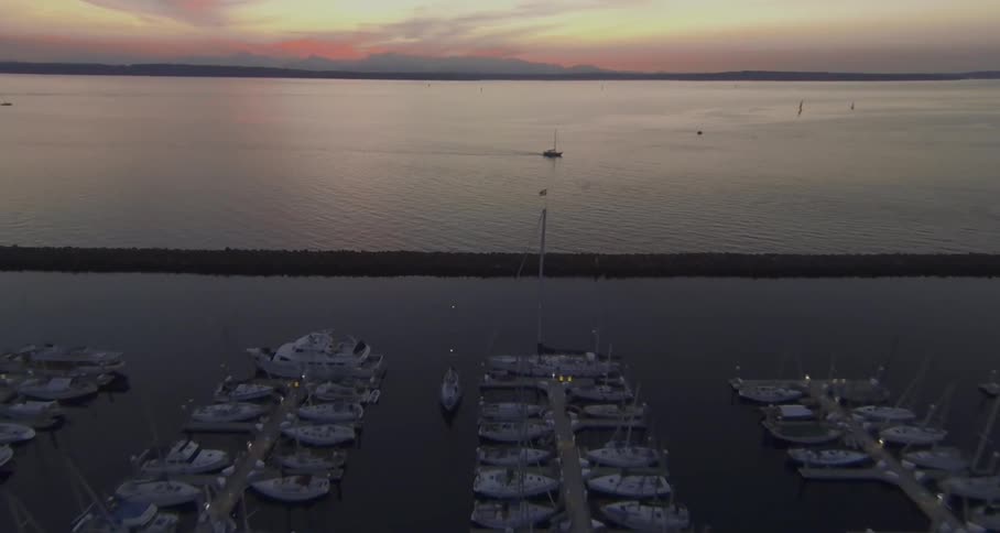 Large body of water at sunset moves to a large dock with many boats