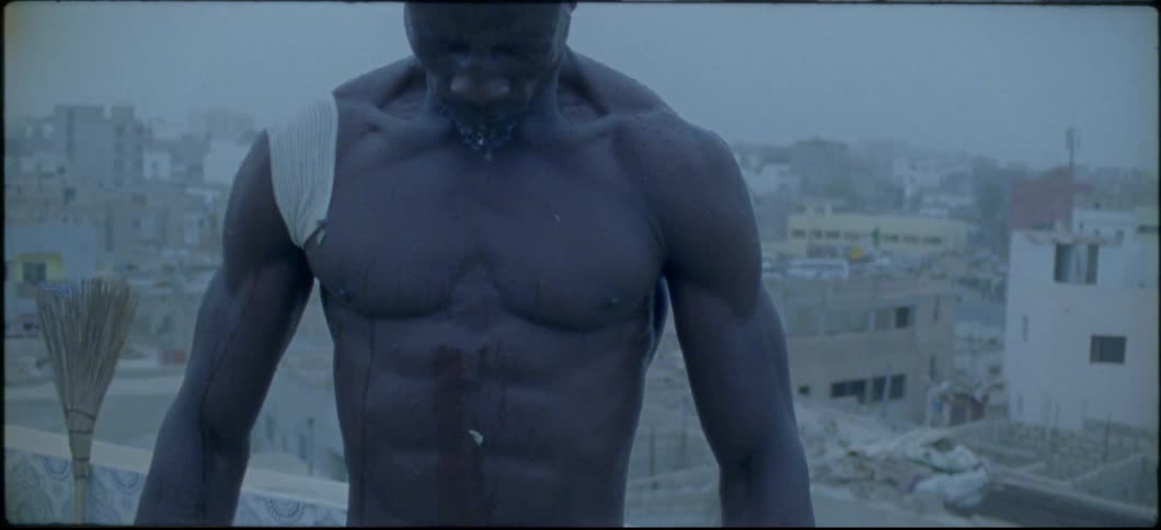 A man without a shirt is standing on a rooftop