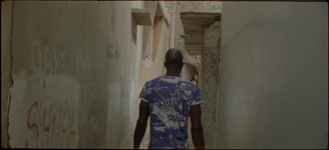 A man is walking down a small alleyway that is full of small rocks