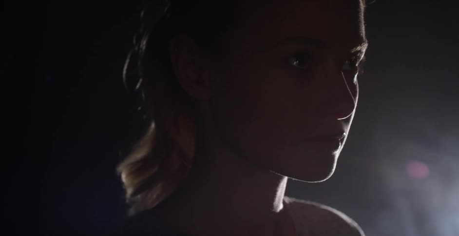 A young woman stands in the shadows