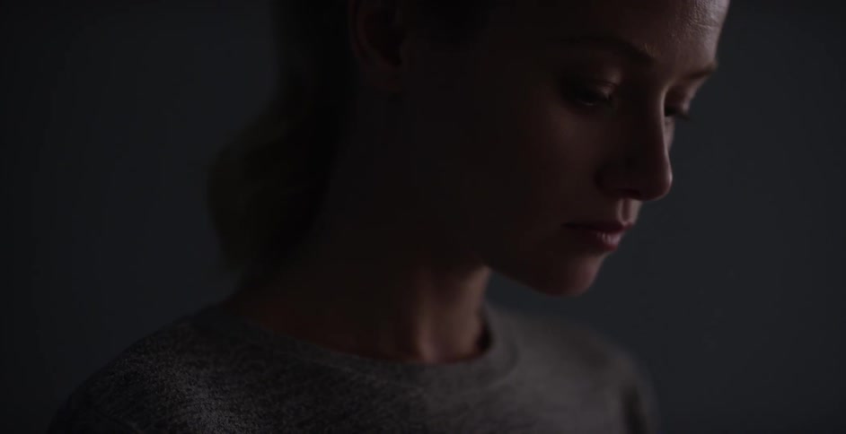 Solemn looking woman in a gray t-shirt in a darkened room