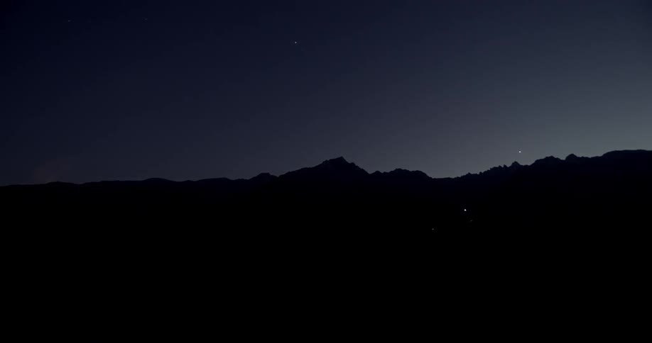 Clouds pass over a mountain range as the sky darkens to night
