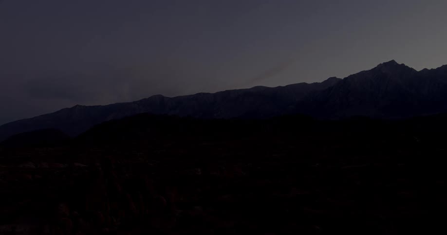 A desert valley with mountains in the distance gets dark at sunset