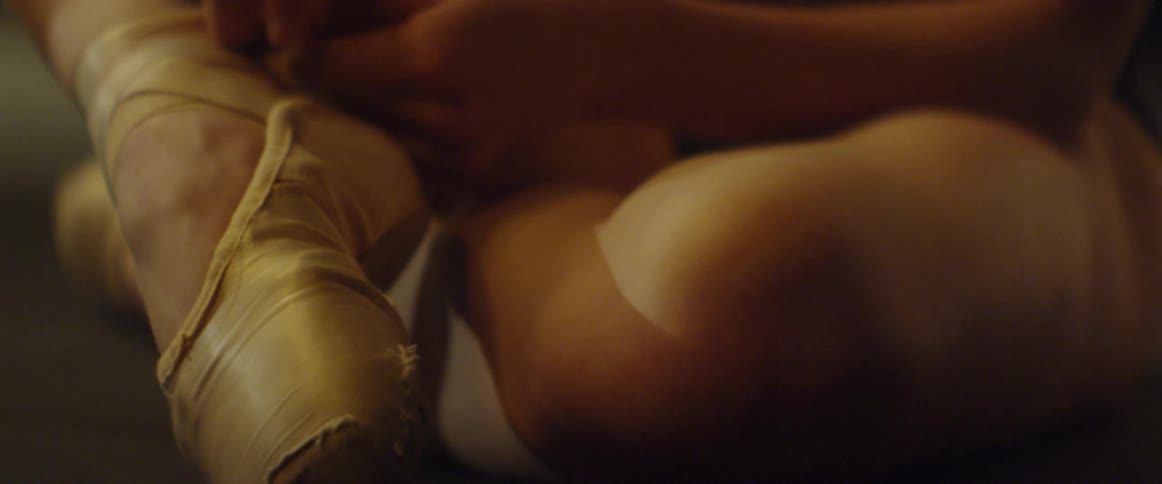 A ballerina sitting on the floor laces her ballet shoes