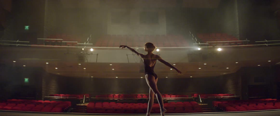 A dancer stretches and practices on stage in an empty theater