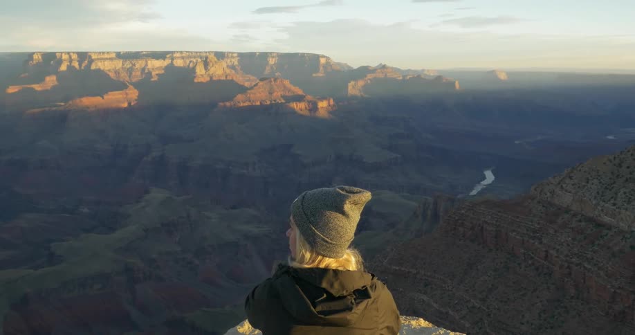 A woman sits on a rock and looks over a canyon