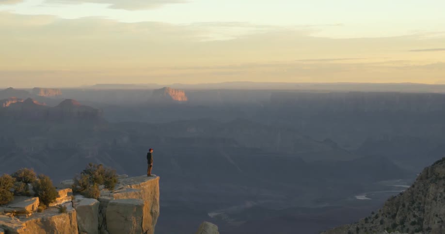 A man stands on the edge of a cliff overlooking a valley