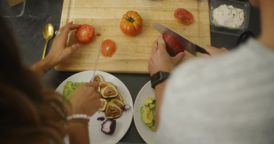 Two people slice tomatoes
