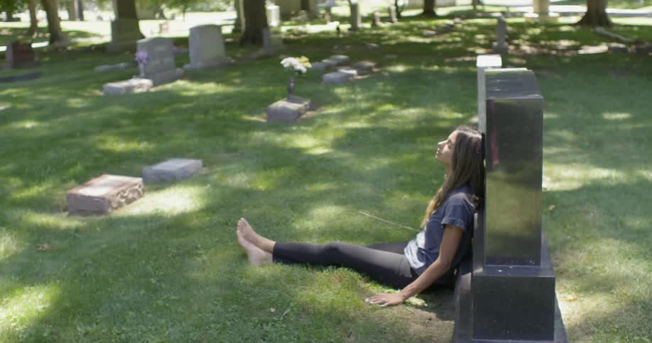 A woman sits and leans against a gravestone