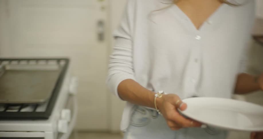 A man passes a plate to a woman as they prepare food in their kitchen