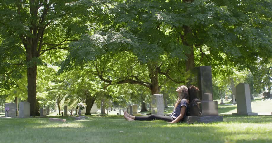Woman sits leaning against a gravestone