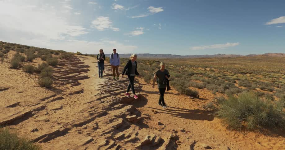 People climbing down from a dirt path and walking towards an area of desert brush