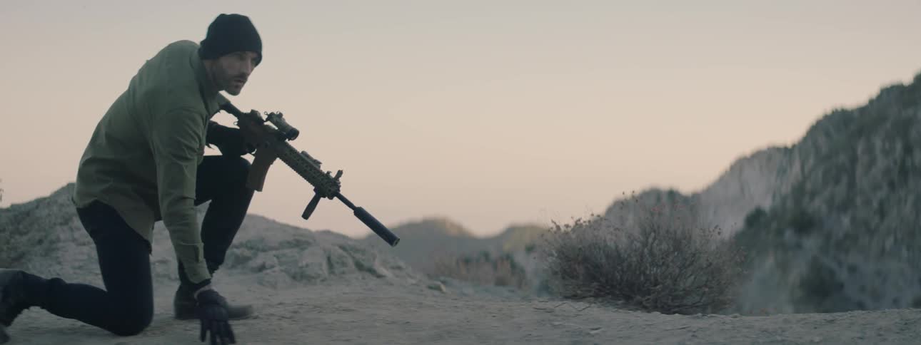 A man carrying a scoped rifle checks a track on the ground