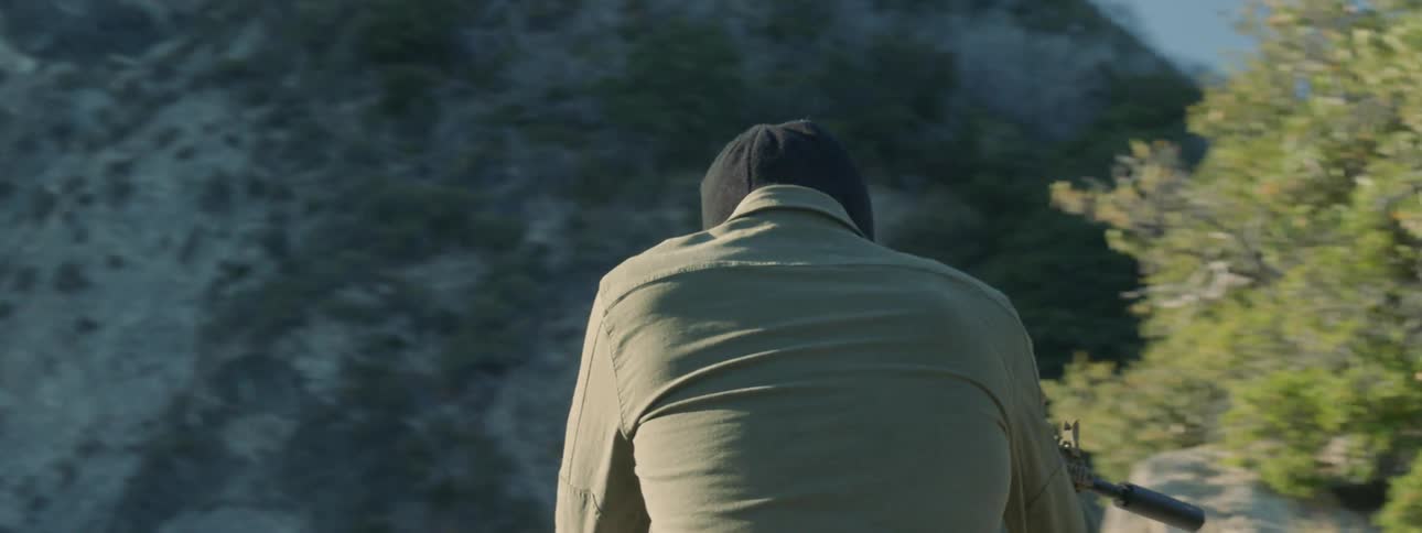 A man brandishes a rifle as he walks in a natural setting