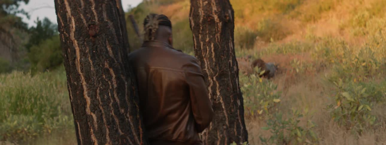 A man carrying a rifle darts into the cover of a tree and aims behind him