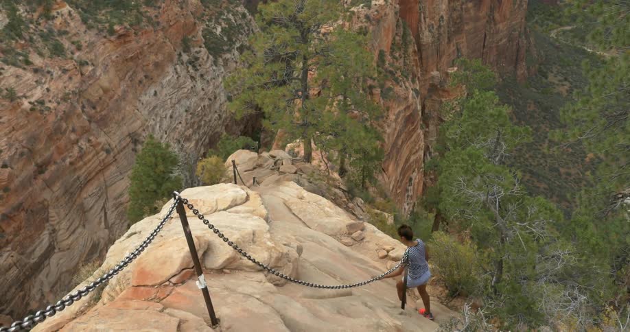 Woman goes around a barrier to walk towards the edge of a mountain