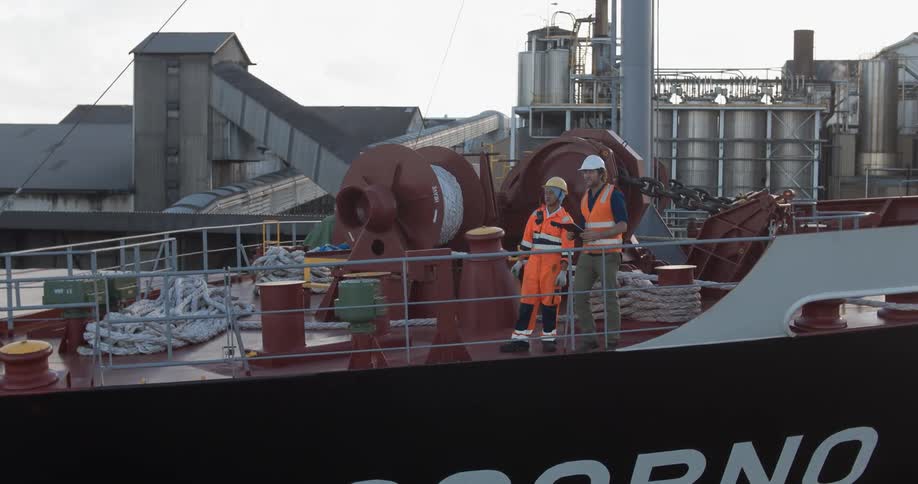 Two men stand on the deck of a ship having a discussion during the day