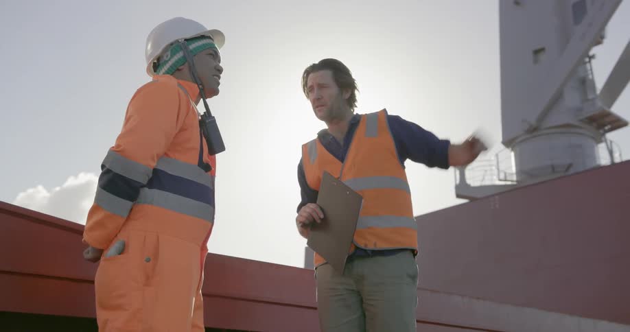 Two workers talk while standing on a ship