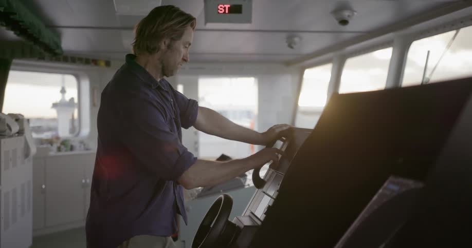 A man taps on the screen of controls on a ships bridge