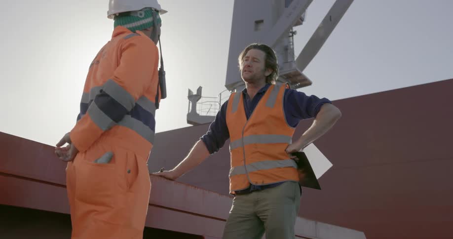 Two men wearing orange stand on a ship on a sunny day