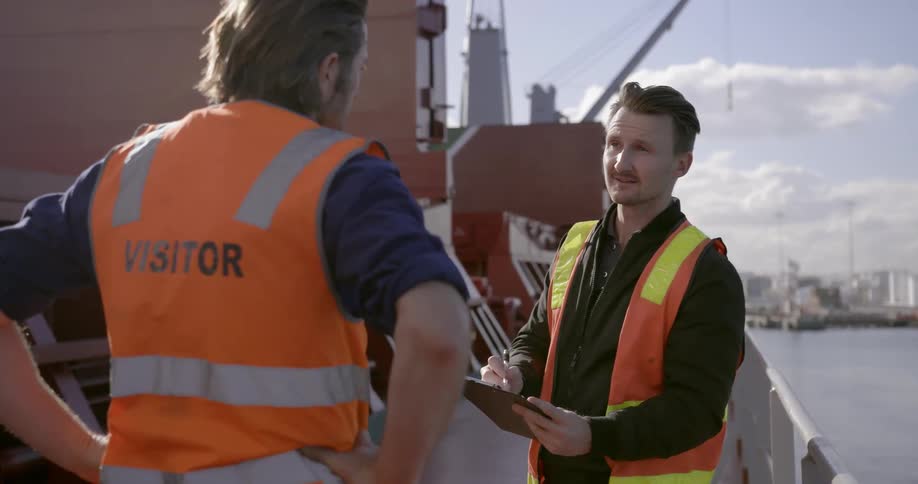 Two men stand on the deck of a ship having a discussion during the day