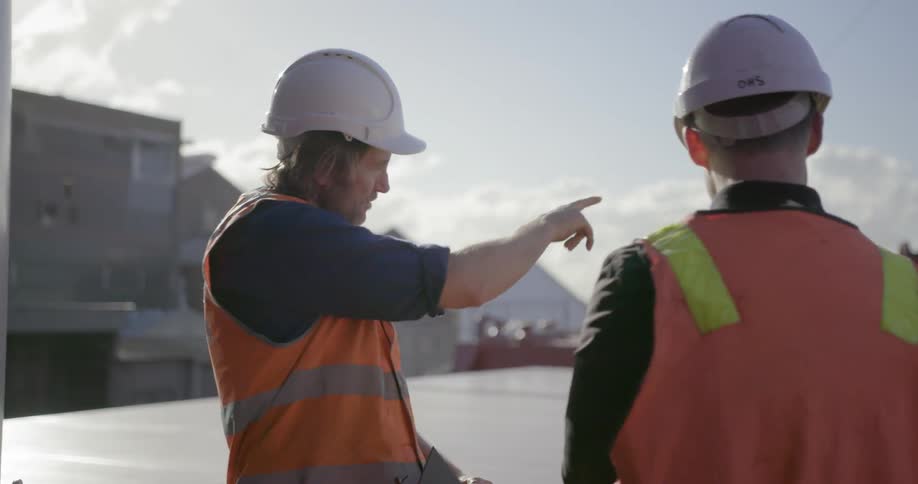 Two workers talk while wearing safety helmets outside