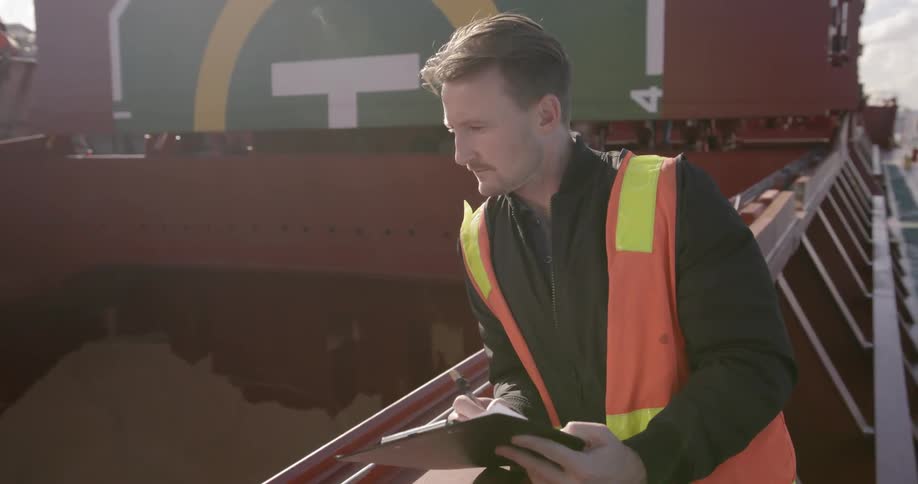 An inspector examines a large ship and writes on a clipboard