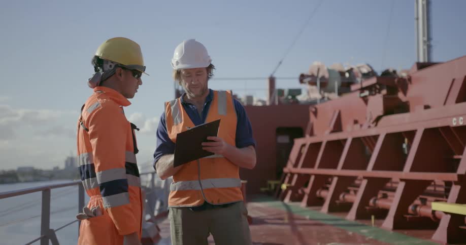 Two men wearing orange stand on a ship on a sunny day
