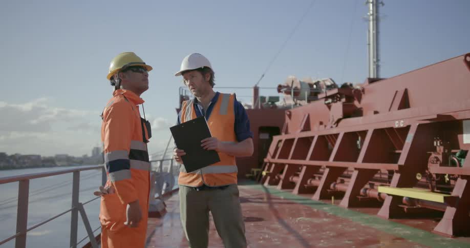 Two construction workers talk on a ship deck