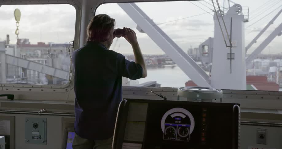 A man is using binoculars and looking over the deck of a ship