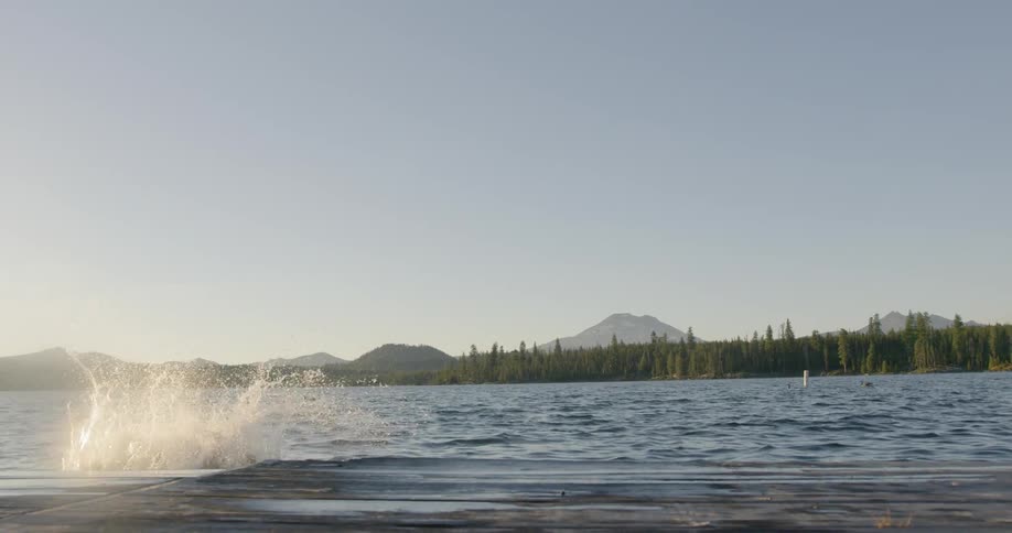 Man jumps off of a dock and into a lake at sunset