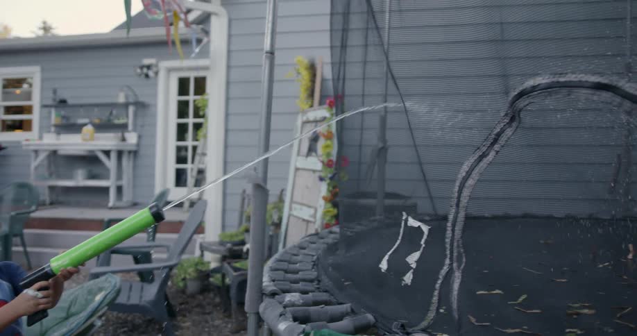 Young boys play in a backyard with a squirt gun and trampoline