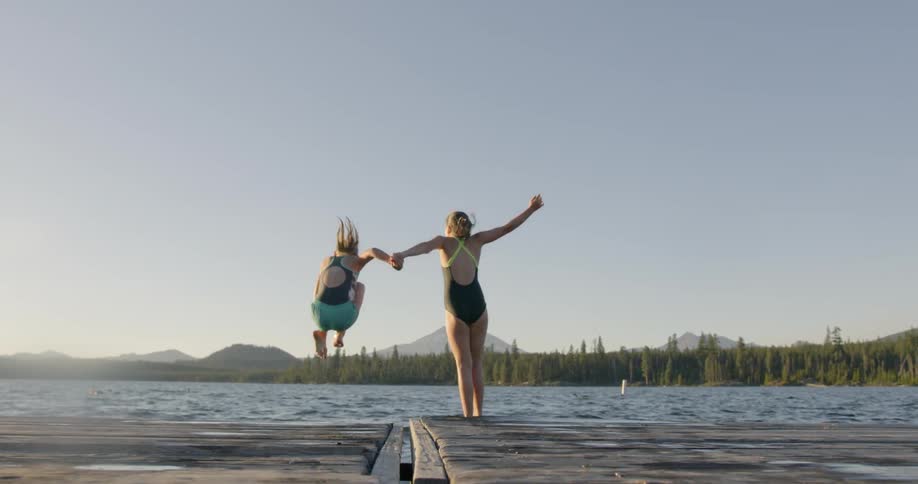 Two girls are jumping into a lake from a dock