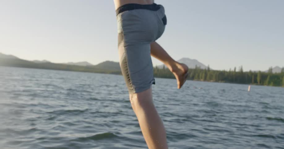 A boy leaps off a pier into a lake on a sunny day