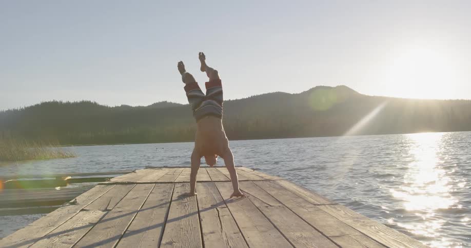 A boy is walking on his hands on a pier on a sunny day