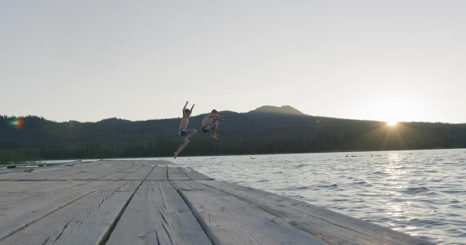 Two kids are running and jumping off a dock into a lake