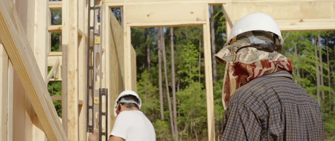 A man at a construction site places a level against a wall frame