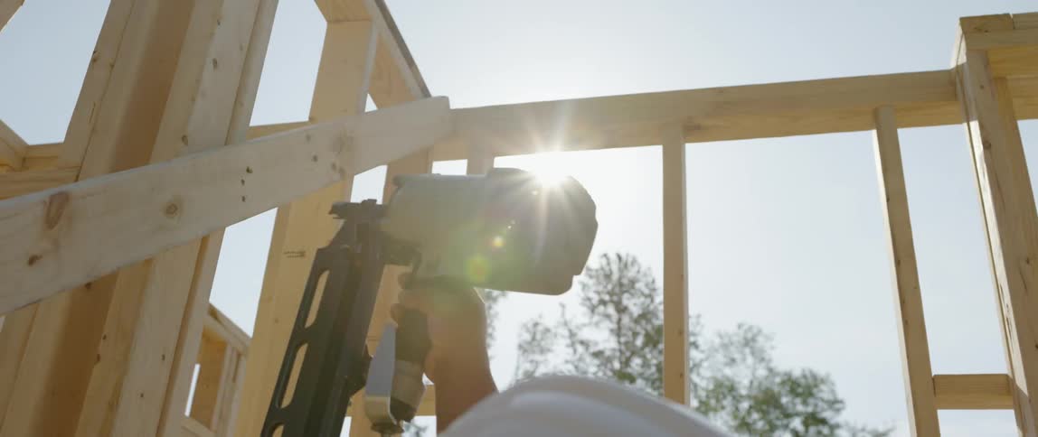 Man uses a nail gun to build assist in building a structure frame
